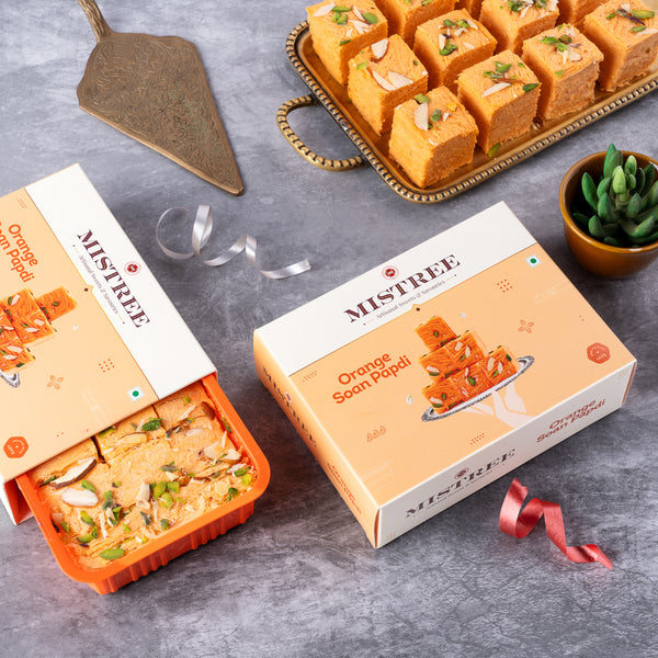 A 250g pack of Orange Soan Papdi, offering a premium traditional sweet experience with a delightful citrus twist.